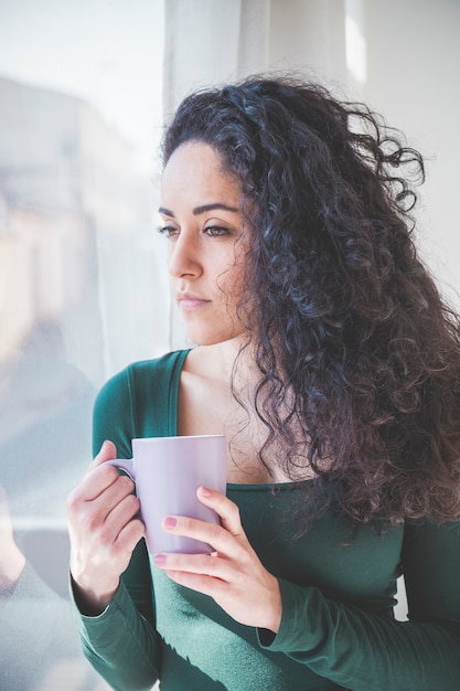 Ragazza malinconica che prende un caffè guardando fuori dalla finestra