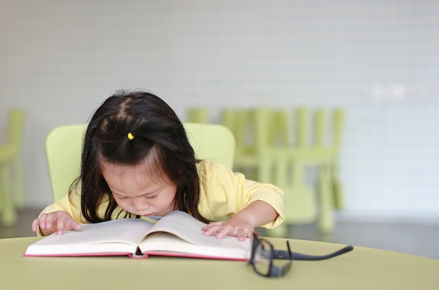 Ragazza miope del miope che legge un libro nella stanza dei bambini.