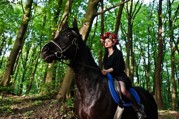 Ragazza mistica che monta un cavallo nero nella foresta