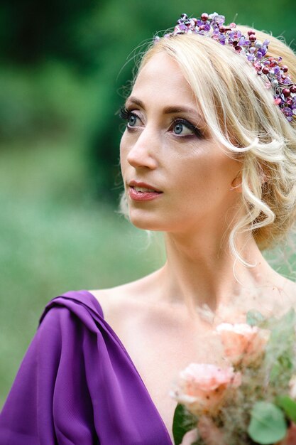 Ragazza modella bionda in un vestito lilla con un bouquet con una foresta verde