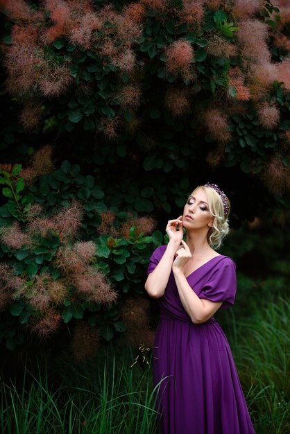 Ragazza modella bionda in un vestito lilla con un bouquet con una foresta verde