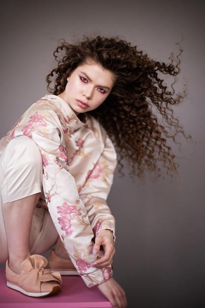 Ragazza modello di moda con capelli sani lucidi ondulati ricci su sfondo grigio Trucco luminoso per la cura dei capelli