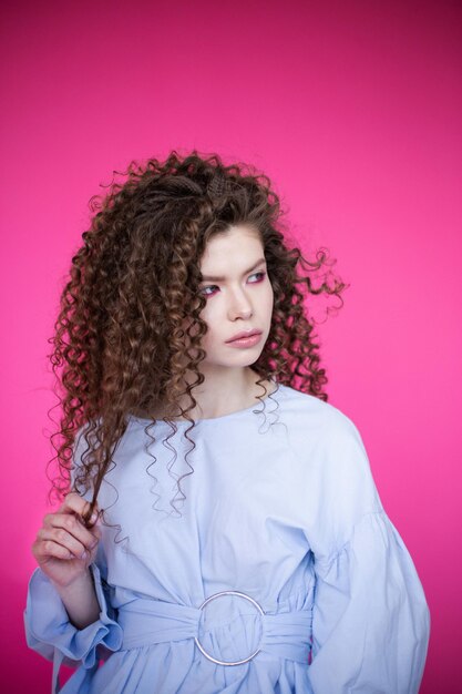 Ragazza modello di moda con capelli sani ricci ondulati lucidi su sfondo rosa Trucco luminoso per la cura dei capelli