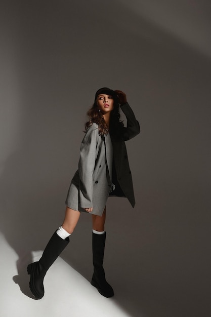 Ragazza modello di moda in un reggiseno blazer oversize alla moda e stivali alla moda su sfondo grigio