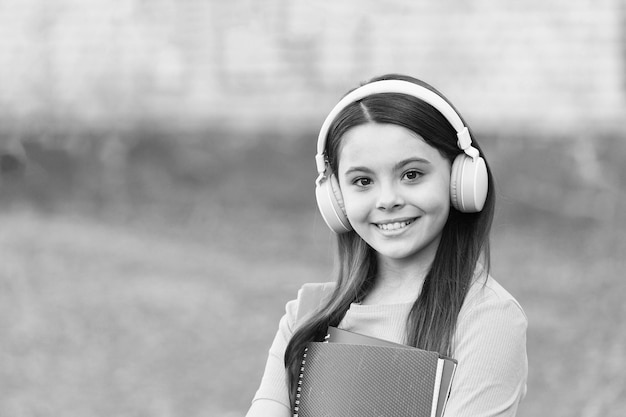 Ragazza moderna del bambino con le cuffie che torna a scuola tiene il concetto di approccio moderno del libro di testo