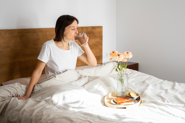 ragazza molto felice che si siede a letto con un caffè tostato e biscotti per colazione