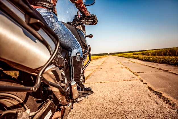 Ragazza motociclista in sella a una moto. Vista dal basso delle gambe in stivali di pelle.