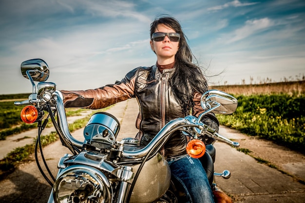 Ragazza motociclista in una giacca di pelle su una moto che guarda il tramonto.