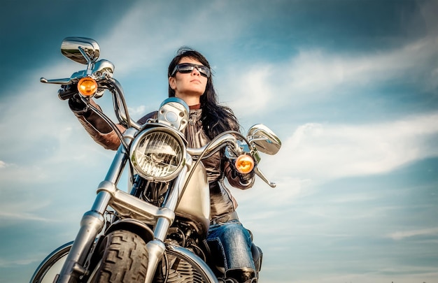 Ragazza motociclista in una giacca di pelle su una moto guardando il tramonto.