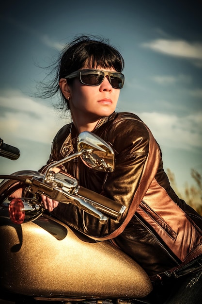 Ragazza motociclista in una giacca di pelle su una moto guardando il tramonto.
