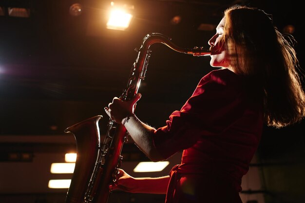 Ragazza musicista in un vestito rosso con un sassofono sul palco