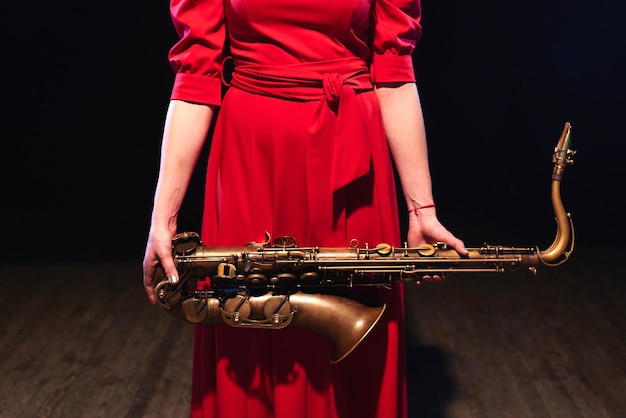 Ragazza musicista in un vestito rosso con un sassofono sul palco