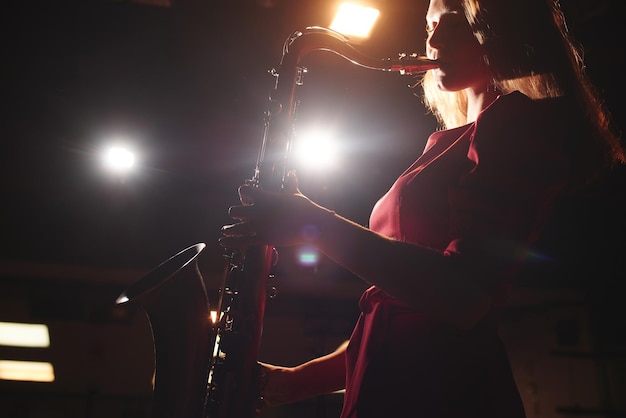 Ragazza musicista in un vestito rosso con un sassofono sul palco