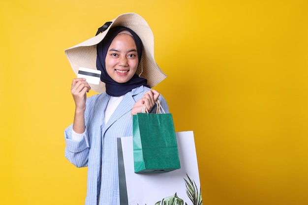 Ragazza musulmana allegra in stile casual che mostra carta per lo shopping mentre trasporta sacchetti di carta