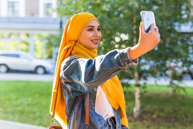 Ragazza musulmana in hijab fa un selfie al telefono in piedi sulla strada della città