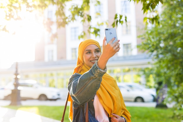 Ragazza musulmana in hijab fa un selfie al telefono in piedi sulla strada della città