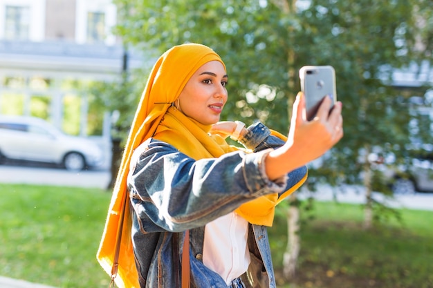 Ragazza musulmana in hijab fa un selfie al telefono in piedi sulla strada della città