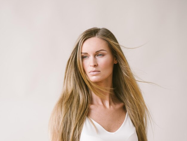 Ragazza naturale del ritratto della bella donna con capelli biondi lunghi sopra la parete grigia bianca. Colpo dello studio.