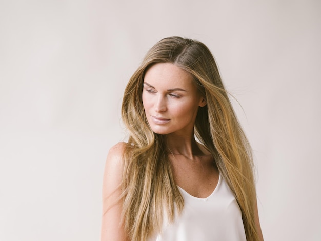 Ragazza naturale del ritratto della bella donna con capelli biondi lunghi sopra la parete grigia bianca. Colpo dello studio.