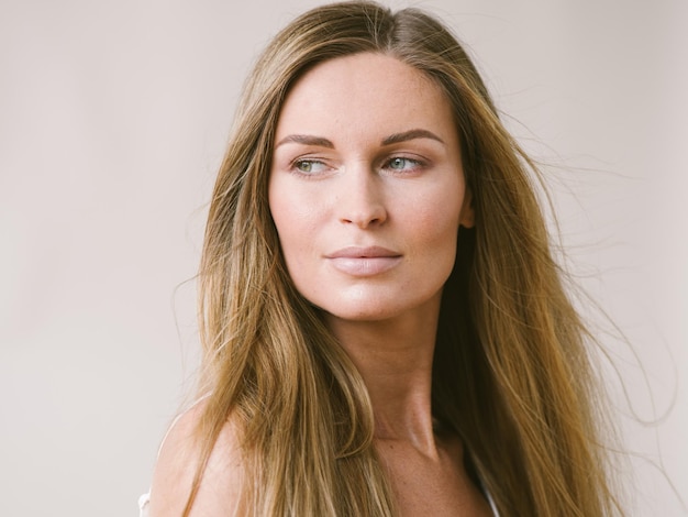 Ragazza naturale del ritratto della bella donna con capelli biondi lunghi sopra la parete grigia bianca. Colpo dello studio.