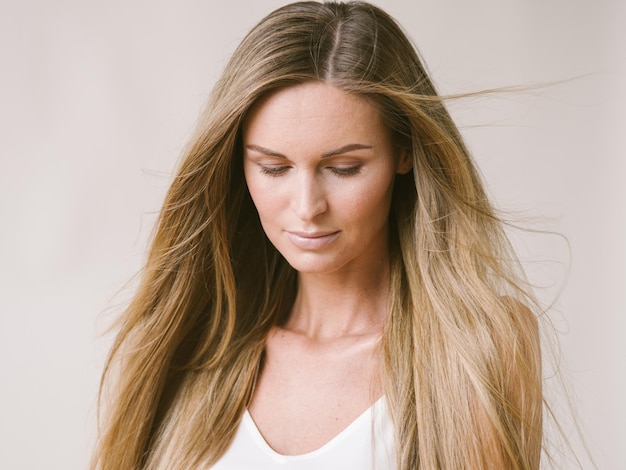 Ragazza naturale del ritratto della bella donna con capelli biondi lunghi sopra la parete grigia bianca. Colpo dello studio.