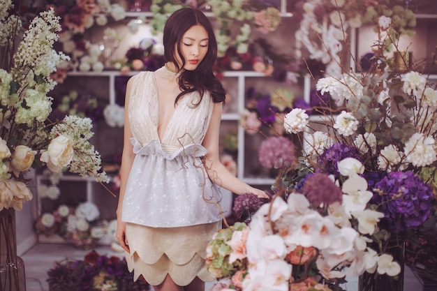 Ragazza nel negozio di fiori. Donna in piedi contro bokeh floreale nel negozio di fiori. Gioioso asiatico