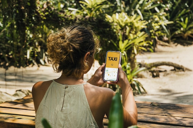 Ragazza nel parco con in mano uno smartphone con l'app Taxi Service sullo schermo. Tavolo in legno rustico. Fornitore di servizi di mobilità in tutto il mondo.