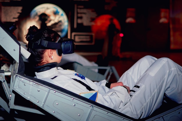 Ragazza nel simulatore spaziale per sastronauti o cosmonauti con un bicchiere di realtà virtuale