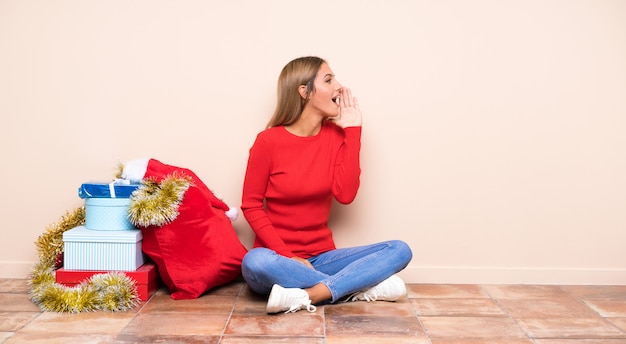 Ragazza nelle feste di natale che si siedono sul pavimento che grida con la bocca spalancata