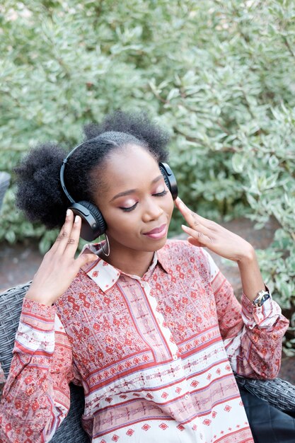 Ragazza nera afro in abito etnico ascoltando musica in cuffia con gli occhi chiusi