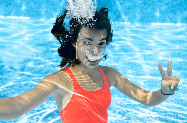Ragazza nuota in piscina sott'acqua, felice adolescente attivo si tuffa e si diverte sott'acqua, fitness per bambini e sport in vacanza in famiglia sulla località