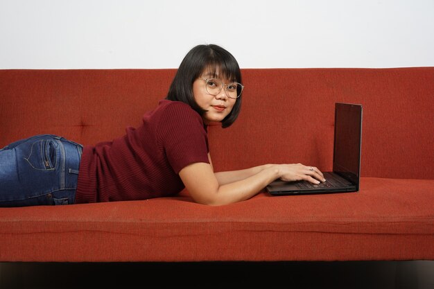 Ragazza o donna indonesiana che usa il laptop per lavorare o lezione online sul divano Donna asiatica