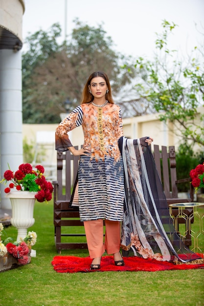 Ragazza pakistana carina che indossa un abito Desi in piedi in giardino con fiori per il servizio fotografico di moda