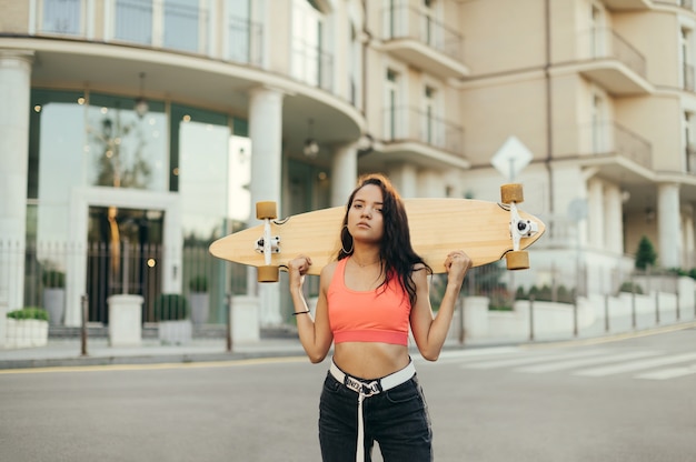 Ragazza pattinatrice in abiti da strada alla moda sta con longboard