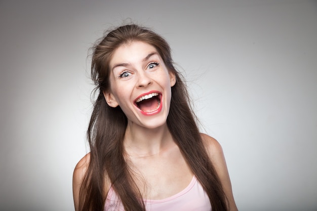 Ragazza pazza che grida forte sul ritratto in studio. Con sfondo grigio vignetta.