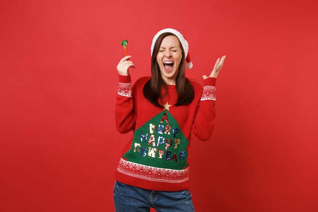 Ragazza pazza di Babbo Natale con gli occhi chiusi che tiene in mano la pipa, allargando le mani, urlando isolata su sfondo rosso brillante. Felice Anno Nuovo 2019 celebrazione festa concetto. Mock up copia spazio.