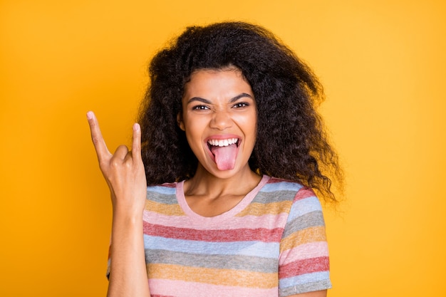 Ragazza pazza di pelle scura con la lingua fuori mostra il simbolo del rock and roll