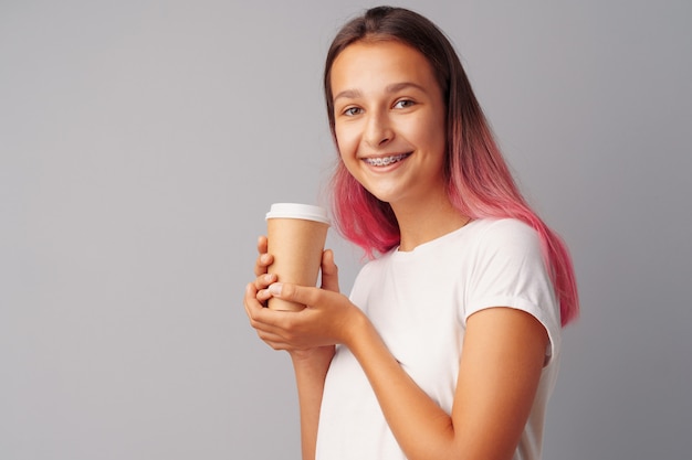 Ragazza piacevole dell'adolescente che tiene una tazza di caffè sopra un fondo grigio