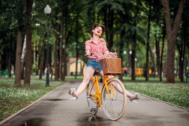 Ragazza pin-up sulla bicicletta retrò, moda americana vintage. Donna carina in stile pinup