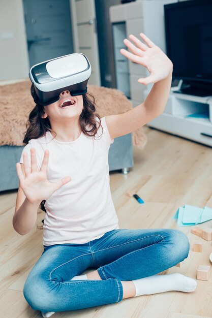 Ragazza positiva che usa i moderni occhiali per realtà virtuale mentre era seduto sul pavimento della sua camera da letto