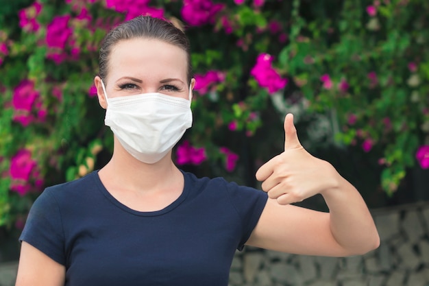 Ragazza positiva felice, giovane bella donna allegra in maschera medica sterile protettiva sul suo viso