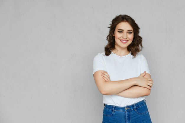 Ragazza positiva in jeans, maglietta bianca e posa rossa degli stiletti