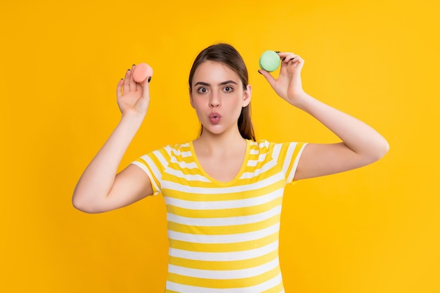 Ragazza positiva stupita con macaron su sfondo giallo