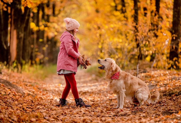 Ragazza preadolescente con cane golden retriever che gioca con foglie gialle al parco autunnale insieme. Bellissimo ritratto di bambino e cagnolino che si diverte all'aperto nella natura