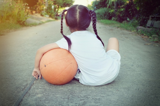 ragazza prescolare con pallacanestro che si siede sulla strada