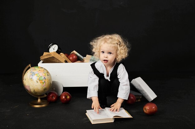Ragazza prescolare felice vicino al carrello con libri, un globo e un orologio su un fondo nero