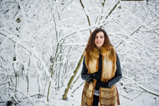 Ragazza riccia di eleganza in pelliccia al parco forestale innevato in inverno.