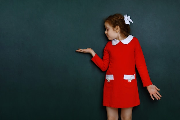 Ragazza riccia intelligente vicino alla lavagna verde in aula.