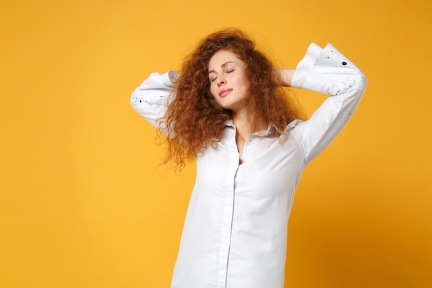 Ragazza rilassata giovane donna dai capelli rossi in camicia bianca casual in posa isolata sul muro giallo arancione