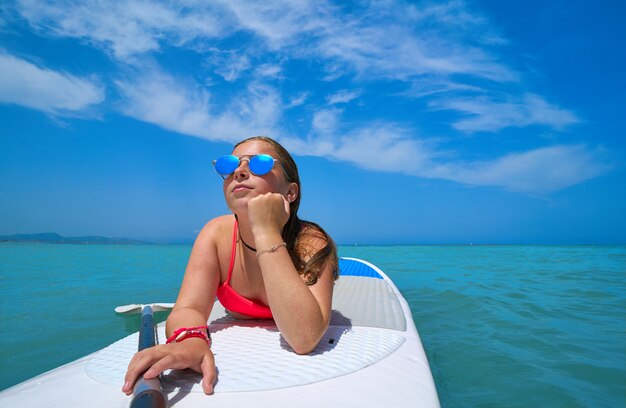 Ragazza rilassata sdraiata sulla tavola da surf paddle SUP